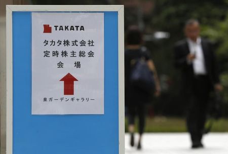 © Reuters. A man walks behind a sign board of Japanese auto parts maker Takata Corp's Annual General Meeting in Tokyo