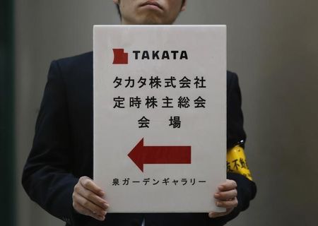 © Reuters. An employee of Japanese auto parts maker Takata Corp holds a sign board of the company's Annual General Meeting at an exit of a station near the venue in Tokyo