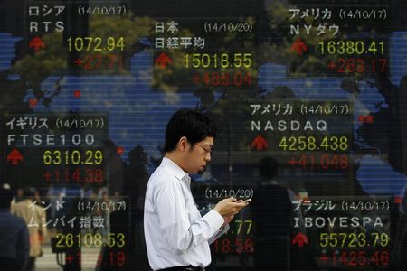 © Reuters. A pedestrian uses his mobile phone as he walks past an electronic board showing the stock market indices of various countries outside a brokerage in Tokyo