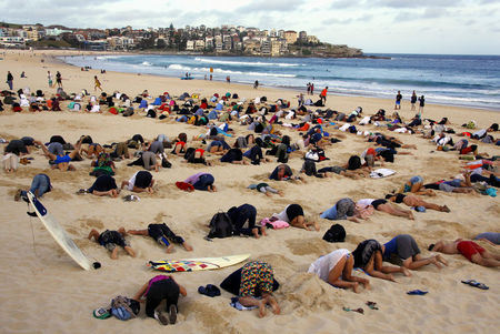 © Reuters. A group of around 400 demonstrators participate in a protest by burying their heads in the sand at Sydney's Bondi Beach