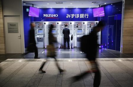 © Reuters. A man uses an ATM machine of Mizuho Bank as pedestrians walk past at a train station in Tokyo