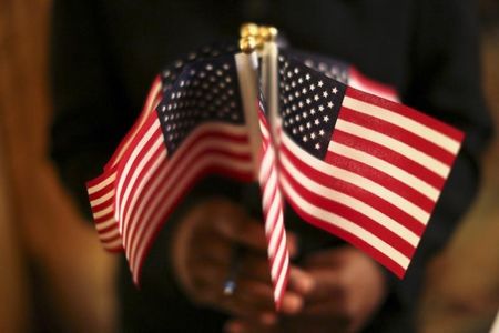 © Reuters. A woman holds a cluster of U.S. flags during a U.S. Citizenship and Immigration Services naturalization ceremony in Oakland