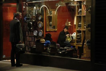 © Reuters. A shop worker looks out at a passer-by from a hat shop in London