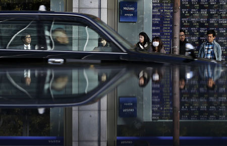 © Reuters. People in front of an electronic board, showing various stock prices, are reflected in a polished stone surface outside a brokerage in Tokyo