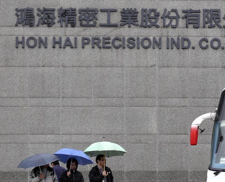 © Reuters. People holding umbrellas walk in front of the headquarters of Hon Hai, which is also known by its trading name Foxconn, in Tucheng, New Taipei city