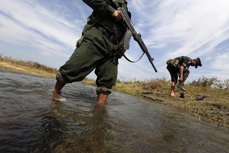 © Reuters. A soldier from the Kachin Independence Army puts on his shoes as he and his comrade cross a stream towards the front line in Laiza
