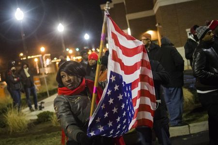 © Reuters. A protester, who was among dozens demanding the criminal indictment of a white police officer who shot dead an unarmed black teenager in August, holds a U.S. flag outside the Ferguson Police Station in Missouri