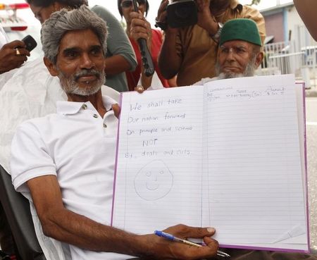 © Reuters. Highway Re-route Movement leader Kublalsingh displays a message he has written in a book on the 13th day of his hunger strike in St Clair