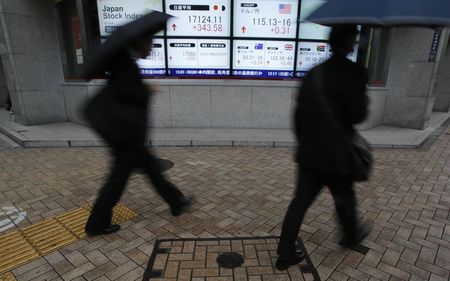 © Reuters. Pedestrians with umbrellas walk past an electronic board showing Japan's Nikkei average and the exchange rates between the Japanese yen and the U.S. dollar, outside a brokerage in Tokyo