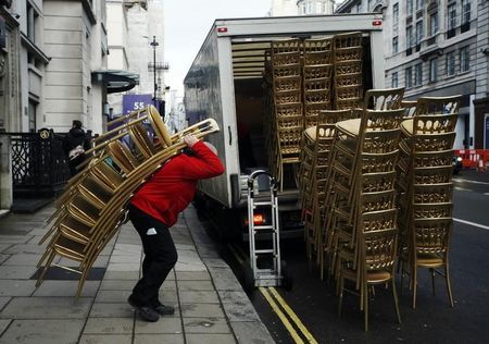 © Reuters. A man loads a van with stacks of gold painted chairs outside a hotel in London