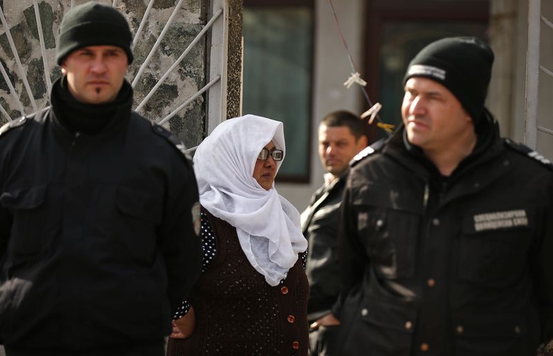 © Reuters. Policemen stand guard outside of a house as a woman looks on in a Roma neighbourhood in the city of Pazadzhik