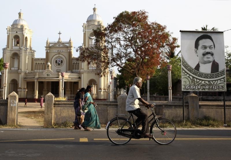 © Reuters. A man cycles past St. James Church and a poster of Sri Lankan President Mahinda Rajapaksa in Jaffna