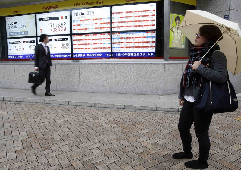 © Reuters. A pedestrian looks at an electronic board showing Japan's Nikkei average and various stock prices outside a brokerage in Tokyo