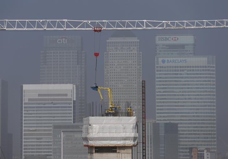 © Reuters. Builders work on a new building being constructed in the foreground of the Canary Wharf financial district, seen from the O2 Arena on a foggy morning in East London