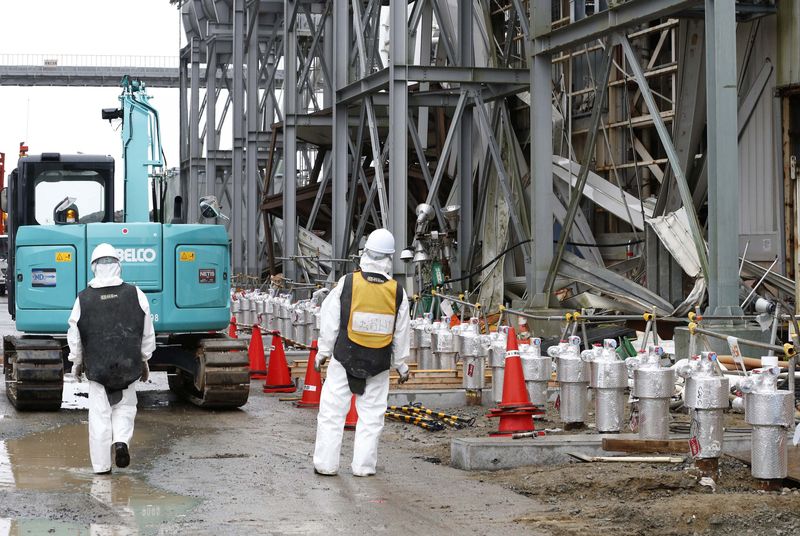 © Reuters. Workers wearing radiation protective gear stand outside of the No. 4 reactor building at TEPCO's tsunami-crippled Fukushima Daiichi nuclear power plant in Fukushima prefecture