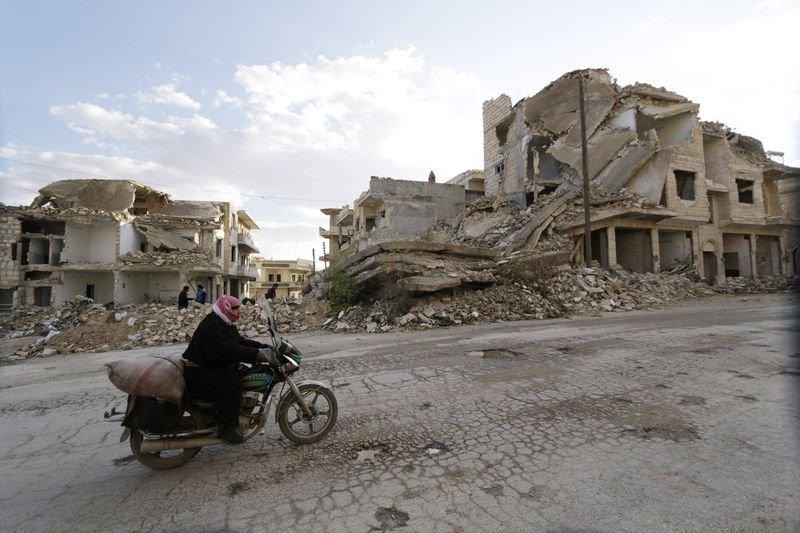 © Reuters. A man rides a motorbike past damaged buildings along a deserted street in Maaret al-Naaman town in Idlib province