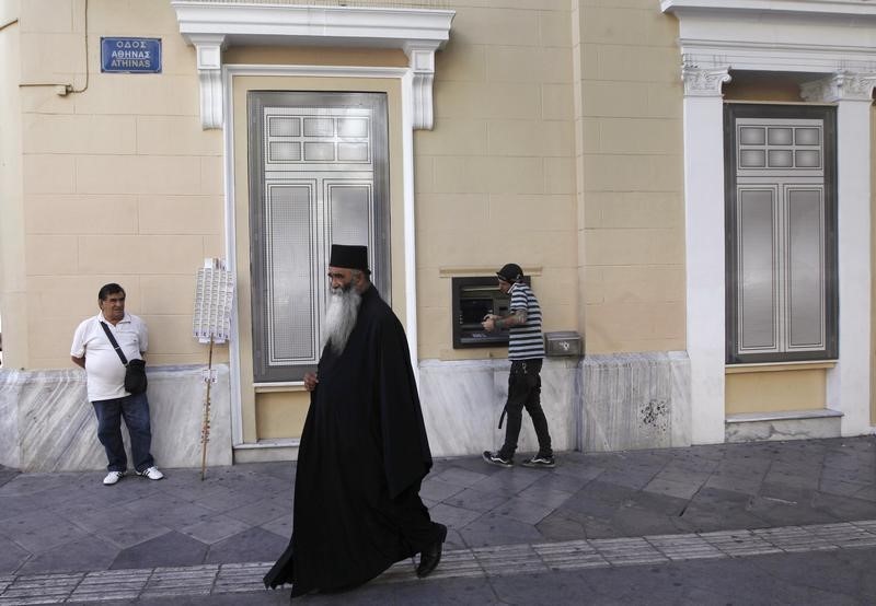 © Reuters. A Greek Orthodox priest walks past a bank branch as a man (R) makes a transactions at an ATM in Athens