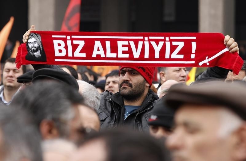 © Reuters. A protester holds a banner reading "we are alevi" as he and many others wait to hear the decision of the court in front of a courthouse in Ankara