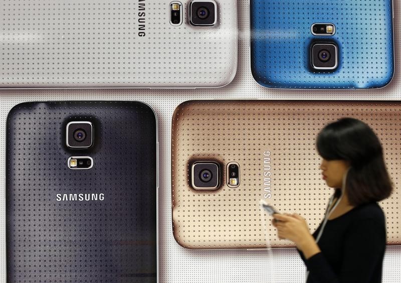 © Reuters. A commuter uses her mobile phone as she walks past a Samsung Galaxy mobile phone advertisement in Singapore