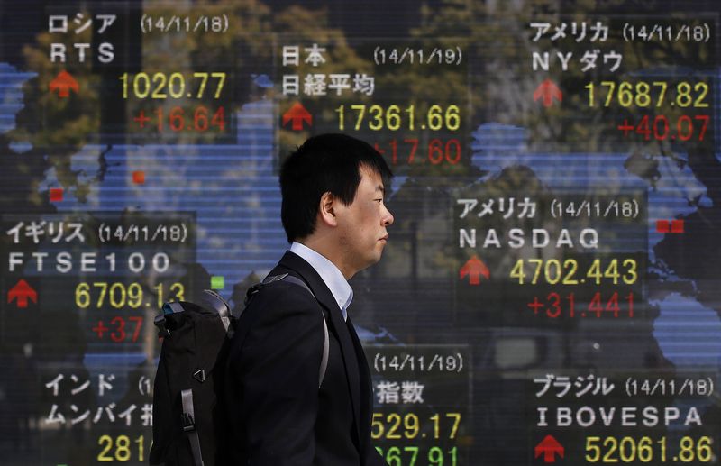 © Reuters. A man walks past an electronic board showing the stock market indices of various countries, outside a brokerage in Tokyo