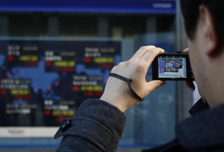 © Reuters. Pedestre tira foto de painel eletrônico com cotações de ações do lado de fora de corretora, em Tóquio