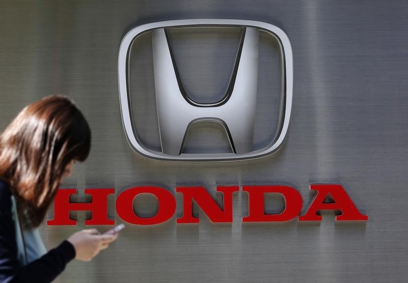 © Reuters. A woman using her mobile phone walks past a logo of Honda Motor Co outside the company's dealership in Tokyo