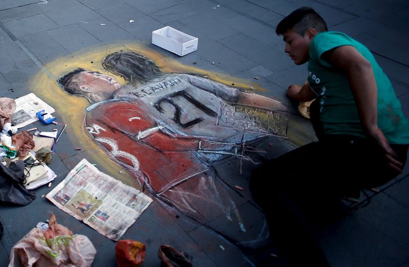 © Reuters. A man draws on the sidewalk a chalk painting of Chile's soccer player Jara and Uruguay's Cavani on the sidewalk in Santiago