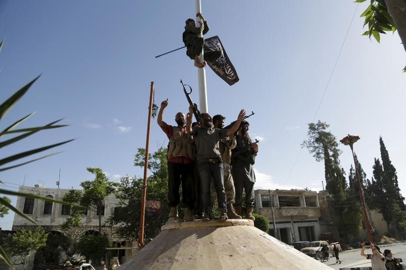 © Reuters. A member of al Qaeda's Nusra Front climbs on a pole to hang the Nusra flag as others celebrate around a central square in the northwestern city of Ariha, after a coalition of insurgent groups seized the area in Idlib province