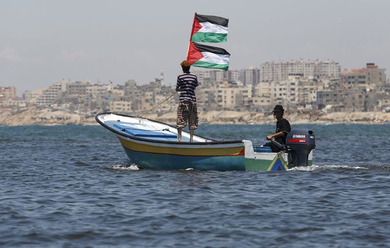 © Reuters. Palestinian man riding a boat holds Palestinian flags during a protest against the Israeli blocking of a boat of foreign activists from reaching Gaza, at the Seaport of Gaza City 