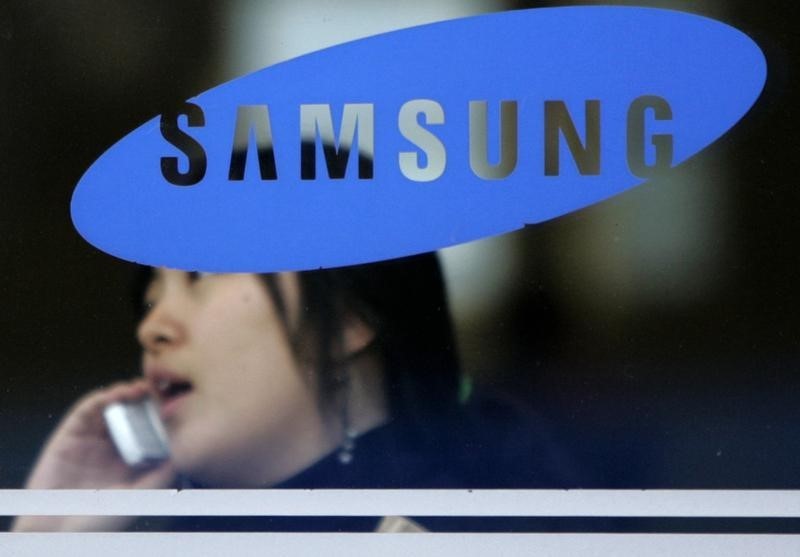 © Reuters. Woman uses her mobile phone behind a logo of Samsung Group in Seoul
