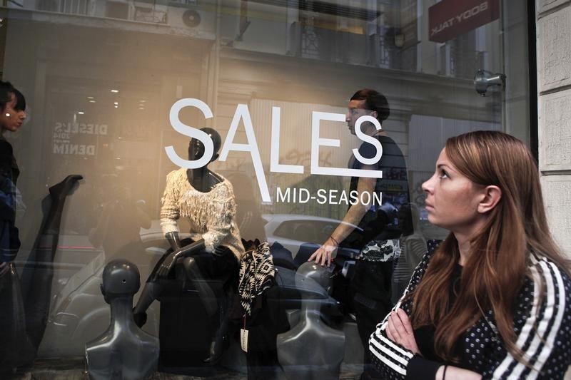 © Reuters. Woman looks at a shop window as employees arrange clothing products in Athens