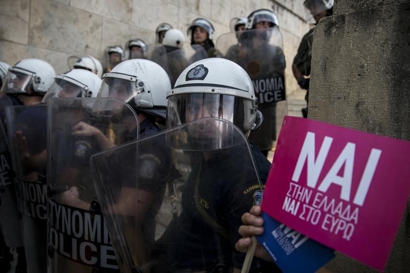 © Reuters. Riot policemen stand guard next to a small flag with the word 'Yes' in Greek during a rally in front of the parliament building in Athens