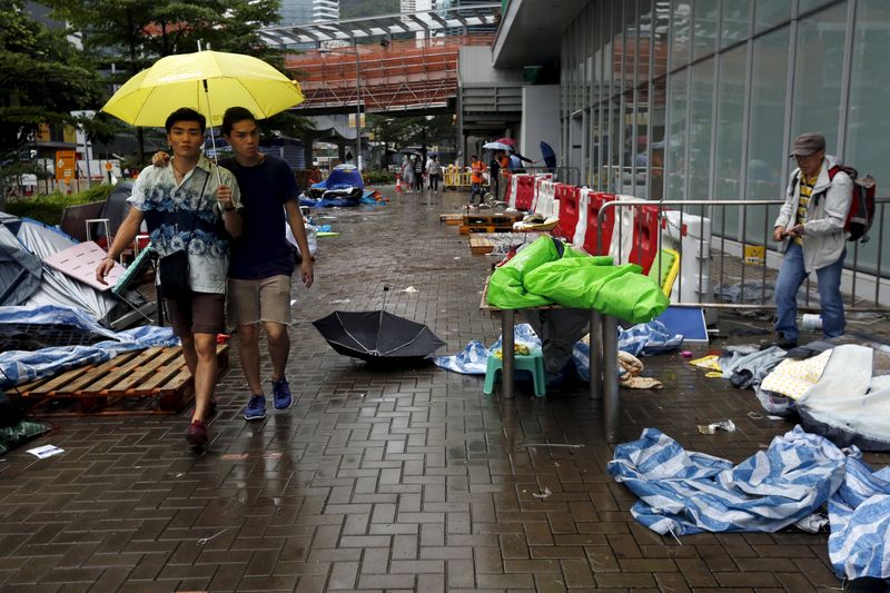 © Reuters. One of the remaining pro-democracy protester packs his belongings as two others carrying a yellow umbrella, the symbol of the Occupy Central movement, walk past outside the government headquarters in Hong Kong