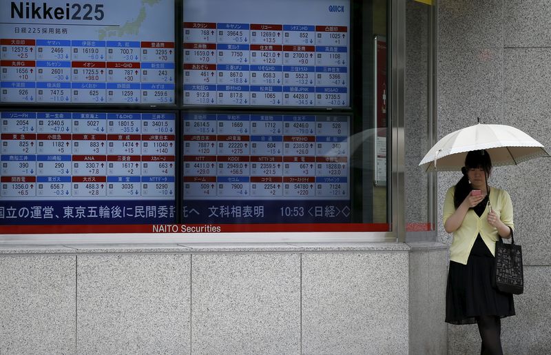 © Reuters. Woman looks at her mobile phone next to a stock quotation board outside a brokerage in Tokyo