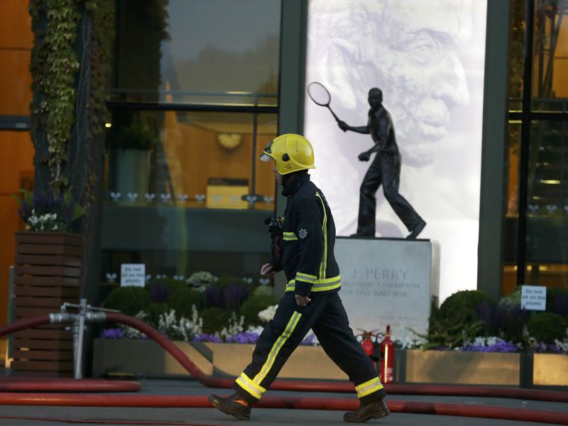 © Reuters. A fireman walks past the statue of Fred Perry after a fire inside Centre Court in Wimbledon at the end of play during the Tennis Championship, in London