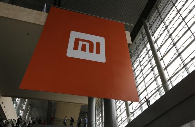 © Reuters. People stand near a logo of Xiaomi ahead of the launching ceremony of Xiaomi Phone 4, in Beijing