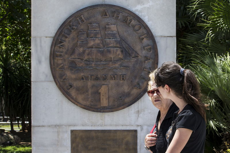 © Reuters. Women walk past a replica of a one drachma coin in Athens