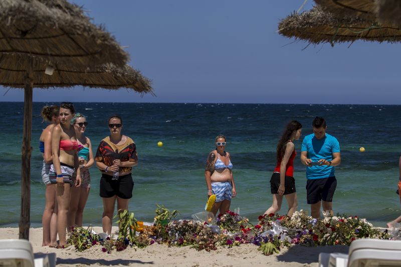 © Reuters. Tourists pay their respects in front of flowers laid out along a beachside in memory of the victims killed by a gunman at the Imperial Marhaba resort