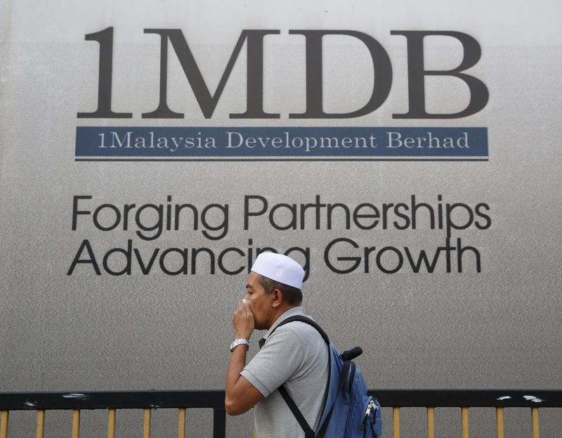 © Reuters. A man covers his mouth as he walks past a 1 Malaysia Development Berhad (1MDB) billboard at the funds flagship Tun Razak Exchange development in Kuala Lumpur, Malaysia