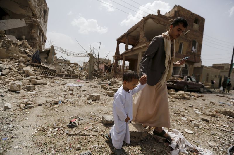 © Reuters. Homem e criança passam por local atingido por ataque em Sanaa