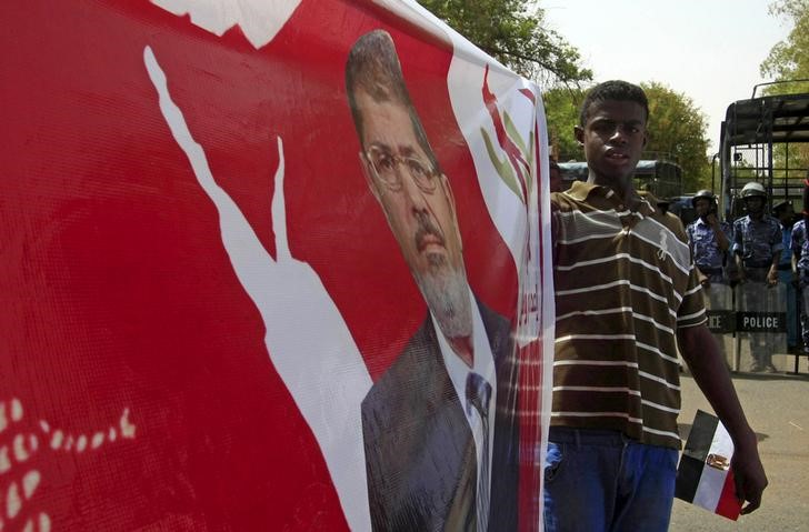 © Reuters. A man holds a banner as protesters from Islamic Movement and Egyptians march against an Egyptian court's decision this week to seek the death penalty for Mursi, in Khartoum