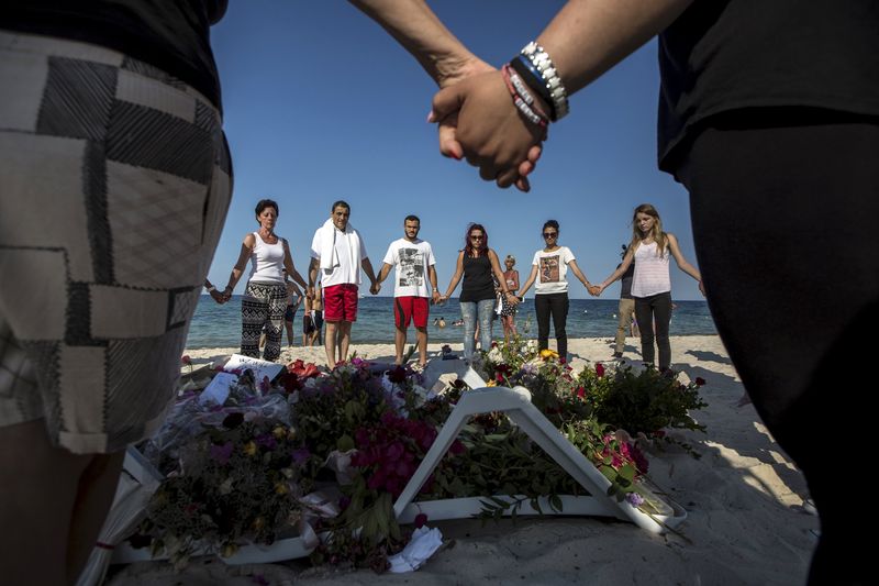 © Reuters. People hold hands as they pray in a circle around bouquets of flowers laid as mementos on the beach of the Imperial Marhaba resort, which was attacked by a gunman, in Sousse, Tunisia