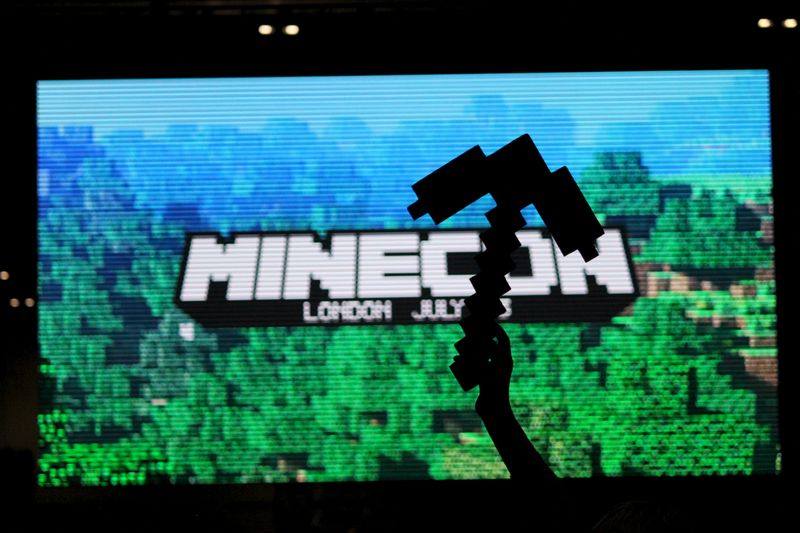 © Reuters. Fan of video game Minecraft waves a foam pick-axe in front of a screen display at the Minecon convention in London