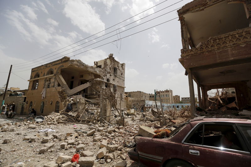 © Reuters. People sit near houses destroyed by a Saudi-led air strike in Yemen's capital Sanaa