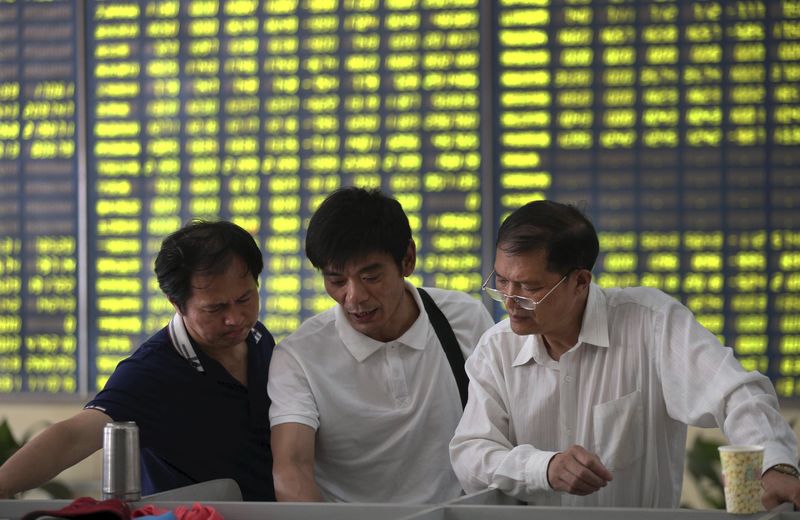 © Reuters. Investors talk in front of an electronic board showing stock information, filled with green figures indicating falling prices, at a brokerage house in Nantong