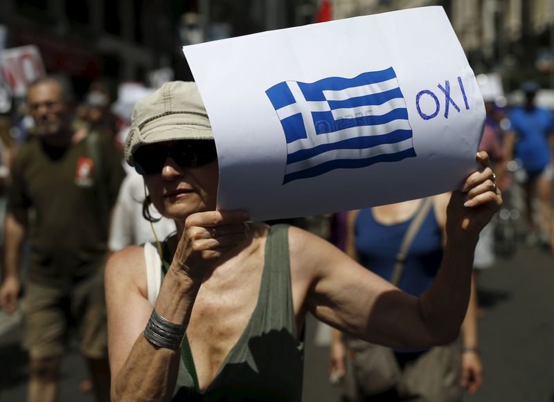 © Reuters. A woman holds a placard with a Greek national flag next to a message in Greek reading, "No" during a rally in support of Greece, in Madrid