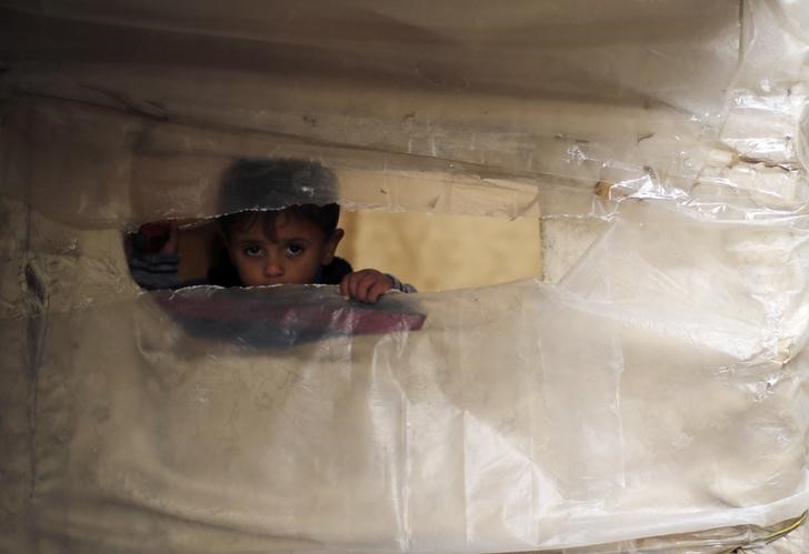 © Reuters. Palestinian boy looks through a hole in a makeshift shelter near his family's house that witnesses said was destroyed by Israeli shelling during a 50-day war last summer, east of Gaza City