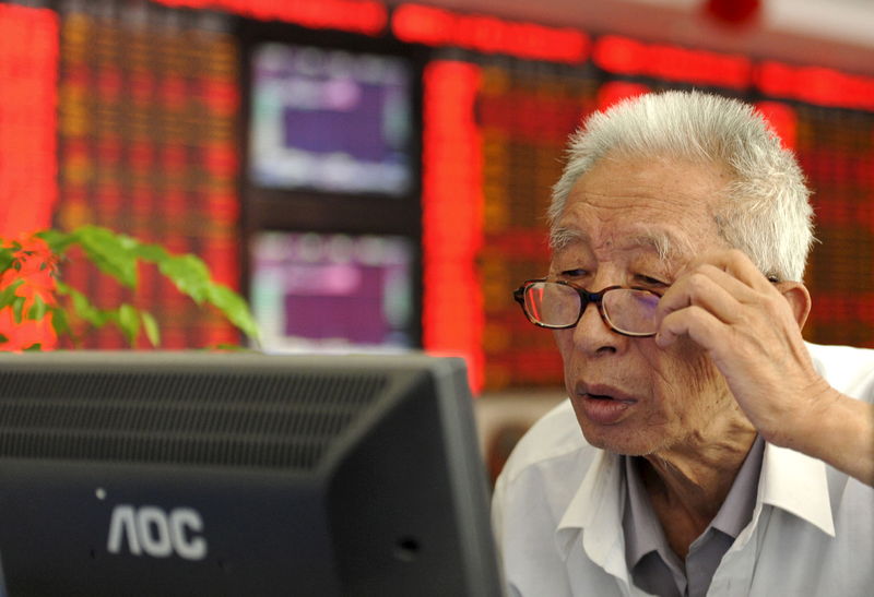 © Reuters. An investor adjusts his glasses as he looks at a computer screen in front of an electronic board showing stock information at a brokerage house in Fuyang