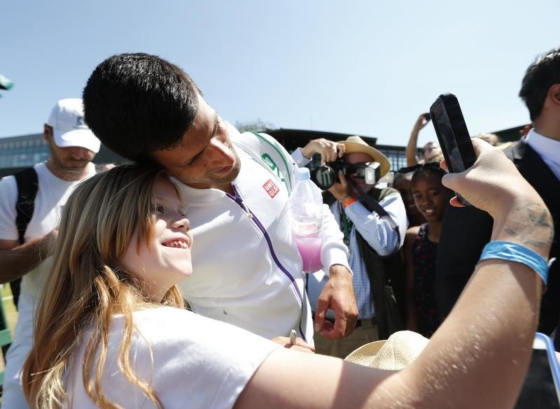 © Reuters. Novak Djokovic of Serbia takes a selfie with a fan after a practice session at the Wimbledon Tennis Championships in London