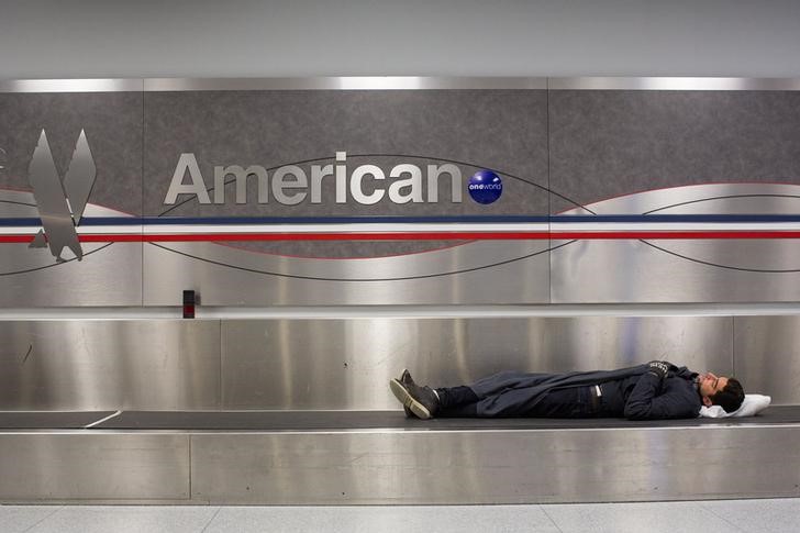 © Reuters. A man sleeps on a conveyer belt under an American Airlines logo at John F. Kennedy International Airport in New York